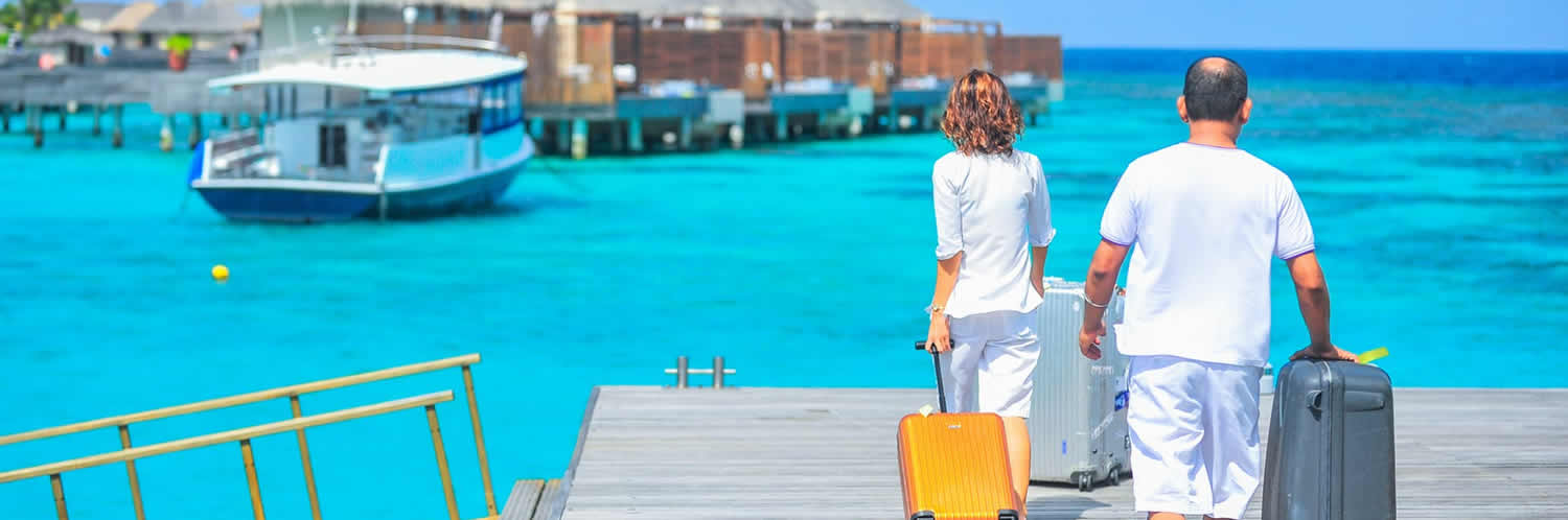 Couple with luggage on tropical dock near boat.