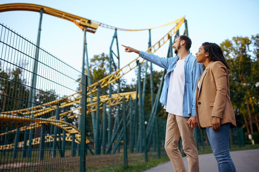 Couple pointing at roller coaster in amusement park.